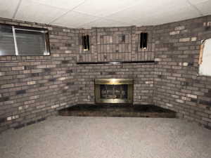 Unfurnished living room with a fireplace, carpet, a paneled ceiling, and brick wall