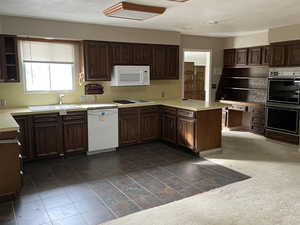 Kitchen with dark brown cabinetry, sink, dark colored carpet, kitchen peninsula, and white appliances