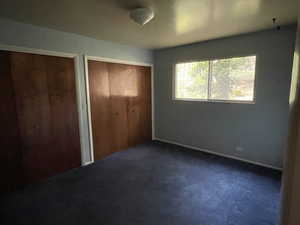 Unfurnished bedroom featuring dark carpet and two closets