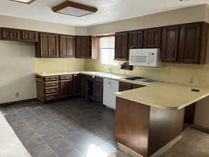 Kitchen with kitchen peninsula, white appliances, dark brown cabinetry, and sink