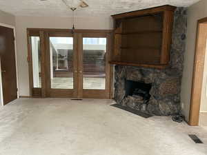 Unfurnished living room featuring a textured ceiling, a fireplace, carpet floors, and french doors