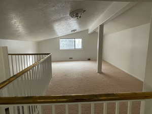 Additional living space with carpet, a textured ceiling, and vaulted ceiling with beams