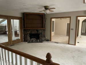 Unfurnished living room with carpet flooring, ceiling fan, a fireplace, and a textured ceiling