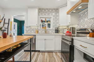 Kitchen featuring sink, white cabinetry, premium range hood, and appliances with stainless steel finishes