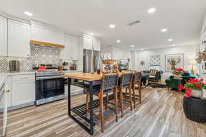 Kitchen with white cabinetry, backsplash, light hardwood / wood-style floors, appliances with stainless steel finishes, and custom exhaust hood