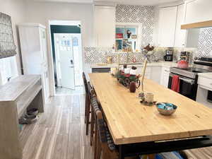 Kitchen with decorative backsplash, sink, light hardwood / wood-style flooring, white cabinetry, and stainless steel electric range