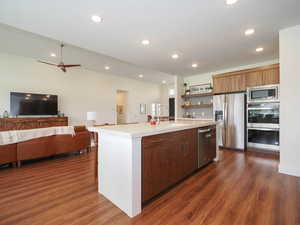 Kitchen with ceiling fan, sink, dark wood-type flooring, a center island with sink, and appliances with stainless steel finishes