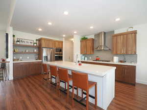 Kitchen featuring appliances with stainless steel finishes, wall chimney exhaust hood, sink, a center island with sink, and dark hardwood / wood-style floors