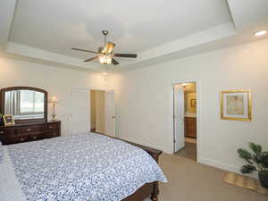 Master bedroom featuring ceiling fan, ensuite bathroom, and a tray ceiling