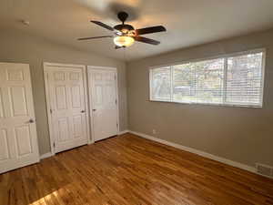 Unfurnished bedroom with hardwood / wood-style floors, lofted ceiling, ceiling fan, and multiple closets