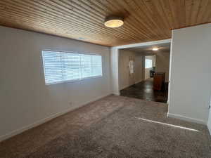 Unfurnished room featuring wood ceiling and dark colored carpet