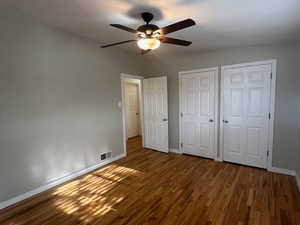 Unfurnished bedroom featuring hardwood / wood-style floors, ceiling fan, and multiple closets