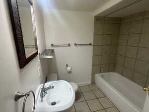 Full bathroom with toilet, tile patterned floors, tiled shower / bath, and sink