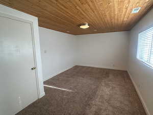 Carpeted spare room featuring wood ceiling