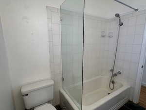 Bathroom with tiled shower / bath combo, toilet, and wood-type flooring