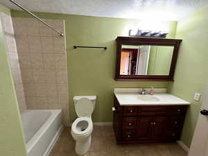 Full bathroom featuring toilet, vanity, a textured ceiling, and tile patterned floors