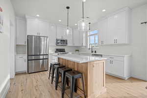 Kitchen featuring hanging light fixtures, stainless steel appliances, a kitchen island, light hardwood / wood-style floors, and white cabinets