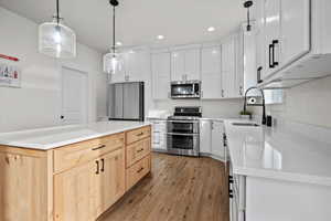 Kitchen featuring sink, light brown cabinets, light hardwood / wood-style flooring, white cabinets, and appliances with stainless steel finishes