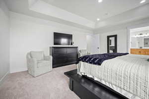 Bedroom featuring light colored carpet, ensuite bath, and a tray ceiling