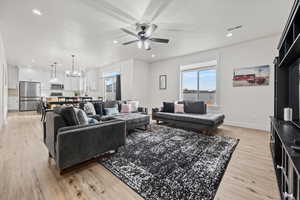 Living room with ceiling fan with notable chandelier and light hardwood / wood-style flooring