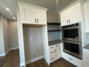 Kitchen featuring stainless steel double oven, white cabinetry, and dark wood-type flooring