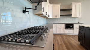 Kitchen featuring decorative backsplash, wood-type flooring, stainless steel appliances, and white cabinetry