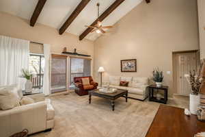 Living room with ceiling fan, light carpet, and high vaulted beam ceiling