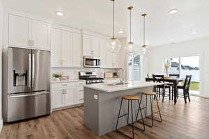 Kitchen featuring sink, an island with sink, decorative light fixtures, white cabinetry, and stainless steel appliances