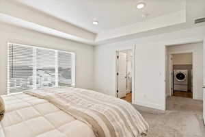 Bedroom with a raised ceiling, light carpet, and washer and clothes dryer