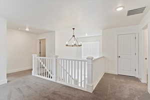 Corridor with light carpet and an inviting chandelier