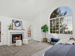 Primary bedroom featuring high vaulted ceiling, light carpet, a tile fireplace and a deck off of primary suite.