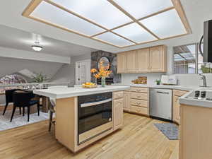 Kitchen with a breakfast bar, light brown cabinetry, brand new appliances with stainless steel finishes, and light hardwood floors