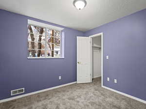 Bedroom #6 with light carpet, a textured ceiling, a closet, and a walk in closet