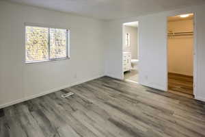 Unfurnished bedroom featuring wood-type flooring, a walk in closet, ensuite bath, and a closet