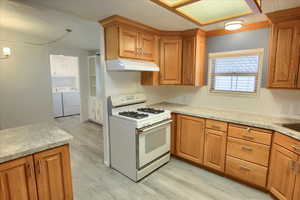 Kitchen featuring washing machine and clothes dryer, white gas stove, and light wood-type flooring