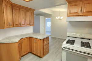 Kitchen featuring ventilation hood, hanging light fixtures, light hardwood / wood-style flooring, white gas stove, and a chandelier