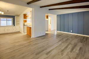 Unfurnished living room featuring vaulted ceiling with beams, light hardwood / wood-style floors, and a notable chandelier