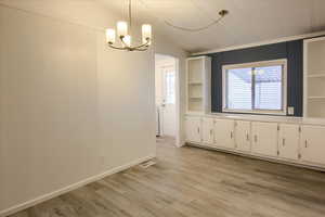 Unfurnished dining area with an inviting chandelier, vaulted ceiling, and light wood-type flooring