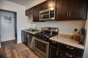 Kitchen featuring light stone countertops, sink, stainless steel appliances, dark hardwood / wood-style flooring, and dark brown cabinets