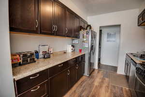 Kitchen with appliances with stainless steel finishes, dark brown cabinetry, hardwood / wood-style flooring, and light stone counters