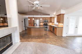 Kitchen featuring appliances with stainless steel finishes, a fireplace, a center island, hanging light fixtures, and lofted ceiling