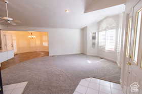 Unfurnished living room featuring ceiling fan with notable chandelier, light colored carpet, and vaulted ceiling