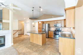 Kitchen featuring a center island, lofted ceiling, hanging light fixtures, stainless steel appliances, and a tiled fireplace