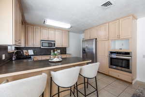 Kitchen with a breakfast bar, sink, light tile patterned floors, kitchen peninsula, and stainless steel appliances