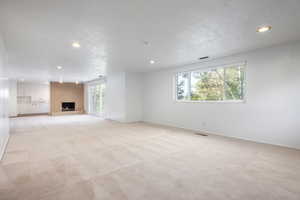 Unfurnished living room with light carpet, a fireplace, a healthy amount of sunlight, and a textured ceiling