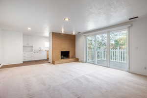 Unfurnished living room with a textured ceiling, sink, a fireplace, and light carpet