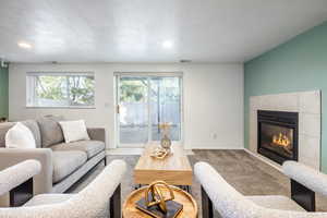 Living room featuring a tile fireplace, light carpet, a textured ceiling, and plenty of natural light