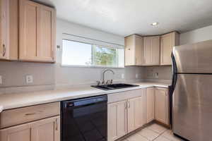 Kitchen with stainless steel fridge, a textured ceiling, sink, light tile patterned floors, and dishwasher