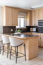 Kitchen with a kitchen bar, a textured ceiling, light brown cabinetry, and tasteful backsplash