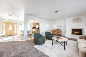 Living room with light colored carpet, a textured ceiling, and a brick fireplace